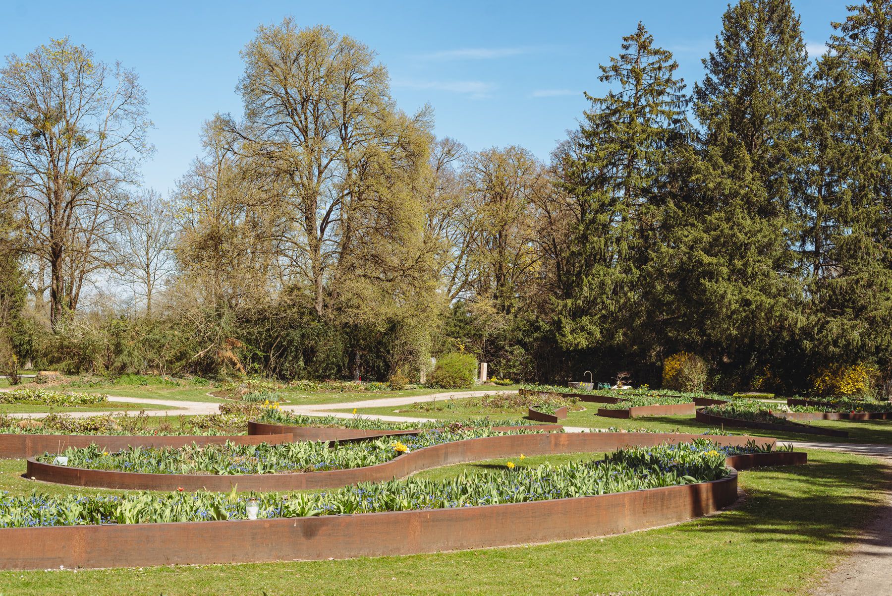 Manicured lawns with curved, edged burial plots beneath mature trees at Obermenzing Cemetery